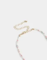 Collar corto de cuentas blancas, celestes y rosadas, con dije de flor blanca con centro azul, dije de caracol y dije de corazón dorado.
