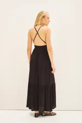 Vestido largo negro con breteles finos, aplique metálico en el escote, espalda baja con breteles cruzados regulables y cierre invisible en la cintura. Tiene un tajo central y volado ancho en el ruedo.