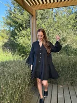 Vestido corto negro de lino, con escote en V, botones frontales y mangas largas acampanadas con volados.