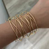 Pulsera dorada con diseño de hilos entrelazados, presenta un estilo moderno y artístico.