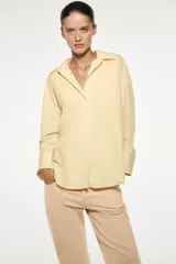 Camisa amarilla de popelina de algodón, con cuello solapa, escote en pico, manga larga con puños y cierre frontal con botones.