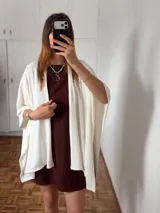 Ruana o poncho de tejido fino color crema o blanco roto, de corte amplio y asimétrico, sin cierres ni cuello definido.