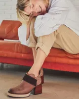 Botín de cuero color marrón con elástico lateral, detalle de cuero con textura animal print en el talón, tira de cuero marrón oscuro sobre el empeine, plataforma y taco de madera.