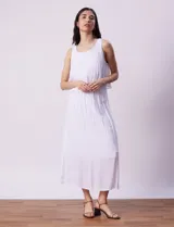 Vestido largo blanco de crepe, con escote redondo y sobrecapa con ruedo de broderie. Corte en la cintura con punto smock.