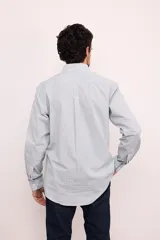 Camisa celeste con rayas verticales blancas, de corte clásico, con cuello abotonado, manga larga y bolsillo en el pecho.