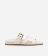 Sandalias planas de cuero sintético color blanco, con puntera redonda y dos tiras, una con hebilla metálica y otra en forma de H.