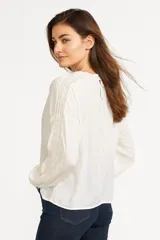 Blusa blanca de algodón con cuello alto con detalles de encaje, mangas largas abullonadas con puños elásticos y bordados calados.
