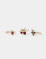 Set de tres anillos dorados con dijes de frutas con incrustaciones de strass: cerezas, frutilla y uvas.