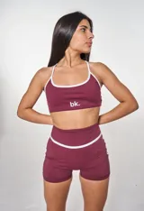 Conjunto deportivo color bordó, compuesto por un top con tirantes finos blancos y logo 'bk.' estampado, y un short ajustado con cintura alta y detalle de línea blanca en el lateral.
