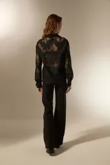 Camisa negra de poliamida con diseño calado de encaje floral, corte holgado, cuello camisero, botones frontales y mangas largas.