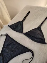 Conjunto de bikini negro con destellos verticales multicolor. El corpiño es de corte triangular con breteles finos regulables y aro metálico en el centro. La bombacha es tipo colaless con tiras laterales regulables.