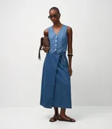 Conjunto de dos piezas de denim azul: un chaleco entallado con botones frontales y una pollera cruzada tipo wrap midi con lazo ajustable en la cintura.