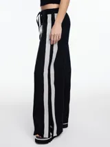 Pantalón de lino negro con elástico en la cintura, tiro medio y calce relajado. Lleva tiras en color gris aplicadas a los laterales, que quedan sueltas en la parte inferior y pueden anudarse.