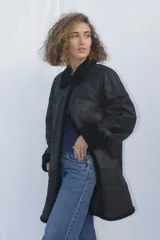 Abrigo gamulán marrón con cuello, solapa, puños y borde frontal de piel sintética blanca. Tiene cierre con botones y bolsillos laterales.