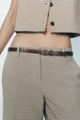 Pantalón de tiro alto con estampado a cuadros en tonos beige y marrón, con bolsillos delanteros y falsos bolsillos traseros. Incluye cinturón marrón con hebilla metálica.
