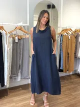 Vestido largo sin mangas color azul claro, confeccionado en lino, con cuello tipo buche o drapeado. Presenta un calce holgado y bolsillos laterales.