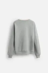 Sudadera gris de tejido compacto con mezcla de algodón y viscosa, corte relaxed fit, cuello redondo y mangas largas. El cuello y los puños tienen acabado en rib combinado a contraste en color crema.