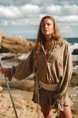 Camisa color beige con rayas verticales finas, bordado de caballo rojo en el bolsillo y cinturón ancho de crochet con lazos.