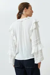 Blusa blanca de bambula con cuello en V y volados en cuello, mangas y frente.