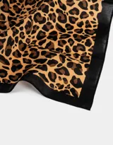 Pañuelo cuadrado de tela satinada con estampado animal print y borde negro.