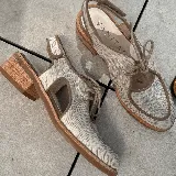 Zapato tipo sueco de cuero vacuno negro con textura reptil, con cordones y talón descubierto. Tiene suela de madera con altura de 4,5 cm en el talón y 1,5 cm en la parte delantera.