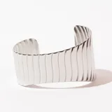 Brazalete rígido plateado con textura acanalada vertical.