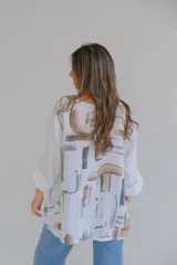 Blusa blanca de lino con estampado abstracto en tonos marrones y grises, de corte holgado y mangas 3/4 con puños abotonados.