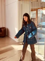 Campera tipo trench de jean con corte oversized y cinto para ajustar. Presenta cuero ovino extra blando en espalda y cuello. Cierre con botones dorados.