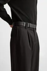 Pantalón negro de corte recto con cinturón de cuero sintético, pliegues frontales, bolsillos laterales y traseros con solapa.