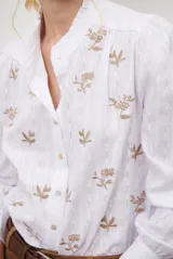 Camisa azul marino con estampado floral en color lila, cuello mao con volantes, cierre frontal de botones y mangas largas abullonadas con puños elásticos.