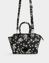 Cartera mini city de cuerina negra estampada con flores blancas. Tiene correa desmontable y doble asa corta.