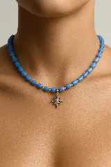 Gargantilla con cuentas cilíndricas de color azul y cuentas transparentes más pequeñas. Dije colgante en forma de estrella de ocho puntas con incrustaciones de circonitas.