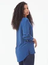 Blusa azul de corte amplio confeccionada en tejido de viscosa, con cuello en V, mangas largas con puños abotonados y aberturas laterales.