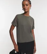 Blusa de color verde militar con cuello redondo y mangas cortas de tul. El cuerpo de la blusa es de media malla con costuras verticales visibles.