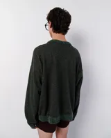 Sweater tejido de lana color verde oscuro con bordado manual en forma de zigzag en tonos blanco, naranja y marrón. Tiene cuello redondo y terminaciones acanaladas en puños y ruedo.