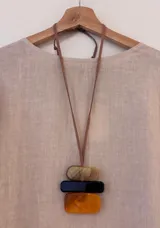 Collar largo con cinta de gamuza marrón regulable y tres dijes rectangulares de acrílico: uno superior color beige con vetas marrones, uno central negro y uno inferior color ámbar.