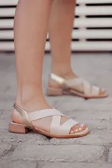 Sandalias bajas color beige con tiras cruzadas y talón descubierto, con elástico dorado en el talón y suela plana.