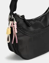 Bandolera hobo negra de tela deportiva con correa regulable, cierre superior, bolsillo frontal y charm lateral decorativo.