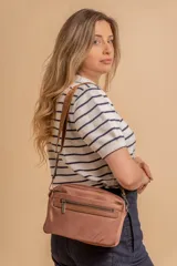 Bandolera color rosa viejo con detalles en cuero marrón claro, múltiples cremalleras metálicas y herrajes plateados. Incluye correa ancha ajustable con el logo de la marca.