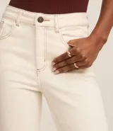 Pantalón slim de jeans color blanco, con cintura mediana, bolsillos delanteros y traseros, cierre con botón y cremallera, y aberturas en el ruedo.