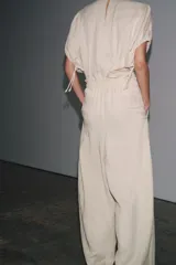 Pantalón palazzo color crudo, confeccionado en tejido fluido con mezcla de lyocell. Presenta tiro medio, cintura elástica ajustable con cordones, bolsillos laterales ocultos en costura y pierna ancha.
