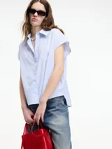 Camisa sin mangas a rayas verticales celestes y blancas, con botones en la parte delantera y trasera, y cuello camisero.