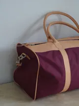 Bolso de lona color negro con detalles en cuero color tostado. Tiene doble asa de mano y correa de hombro ajustable y extraíble.