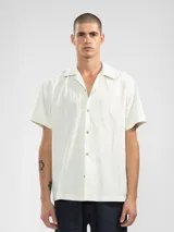 Camisa de manga corta color crema, con cuello camp y calce relajado. Confeccionada en una mezcla de lino y algodón, con botones de madera y parche característico de Polonio.