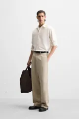 Pantalón color beige de corte ancho, con pliegues frontales, bolsillos laterales y traseros de doble vivo.