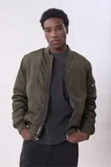Campera tipo bomber color verde militar con cierre frontal, cuello, puños y ruedo acanalados. Incluye bolsillo con cierre en la manga izquierda.