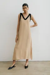 Vestido midi color beige, de corte recto y breteles finos, con escote en V y detalle de volados negros en el escote. Presenta tajos laterales.