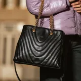 Cartera grande negra de cuero sintético con diseño acolchado en formato rectangular. Tiene acceso con cierre, correa regulable, herrajes dorados y doble compartimento interno con bolsillos. Se puede usar como bandolera.