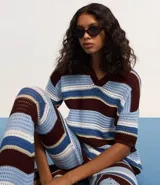 Remera oversized de punto con rayas horizontales en tonos marrón, celeste y blanco. Presenta cuello polo y mangas cortas.