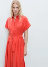Vestido midi camisero color coral con cuello camisero, manga corta, cierre frontal con botones y cinturón con hebilla. Diseño evasé con tablas en la falda.